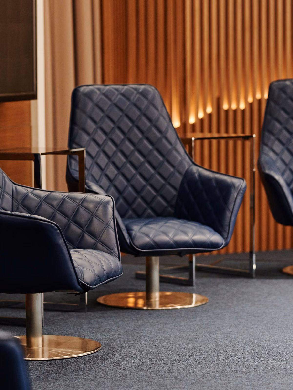 Licensed stock: navy quilted lounge chairs against wood slats — illustrative lifestyle-membership lounge, no logos.